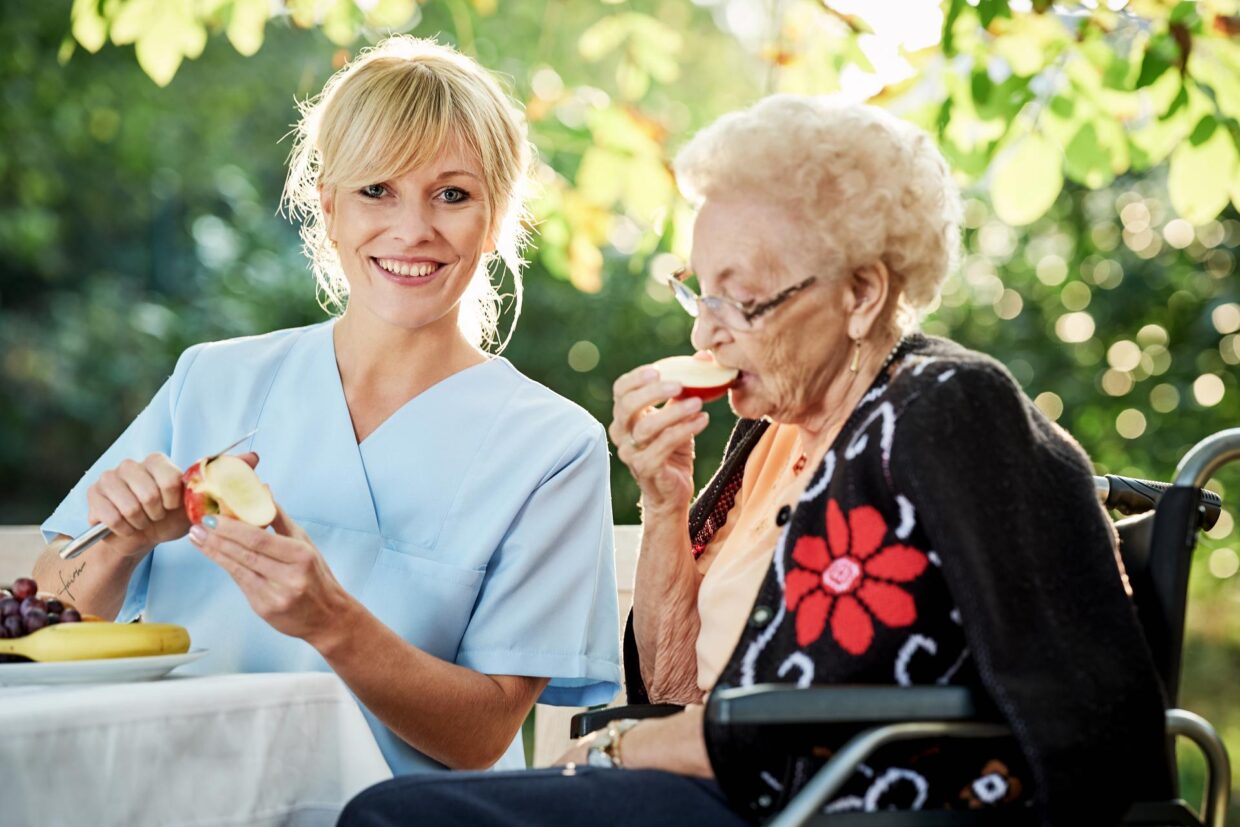 Pflegerin hilft Seniorin beim Obst schälen