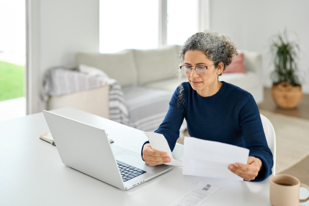 Frau am Laptop prüft Rechnungen und Dokumente in ihrem modernen Homeoffice.