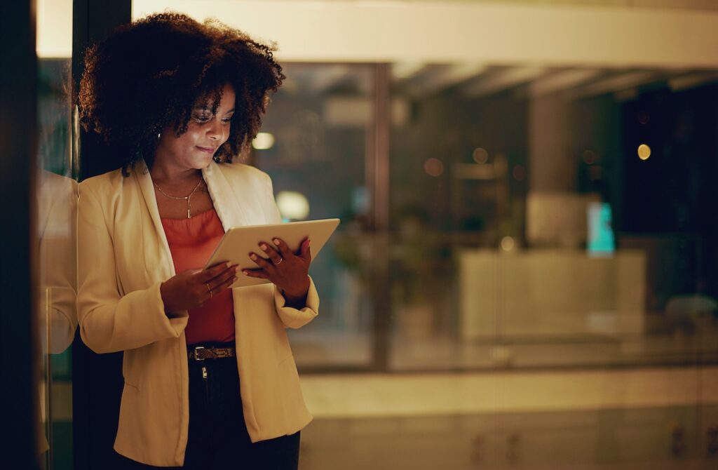 Geschäftsfrau in einem modernen Büro bei Nacht, nutzt ein Tablet zur Bearbeitung von Lohnabrechnungen.