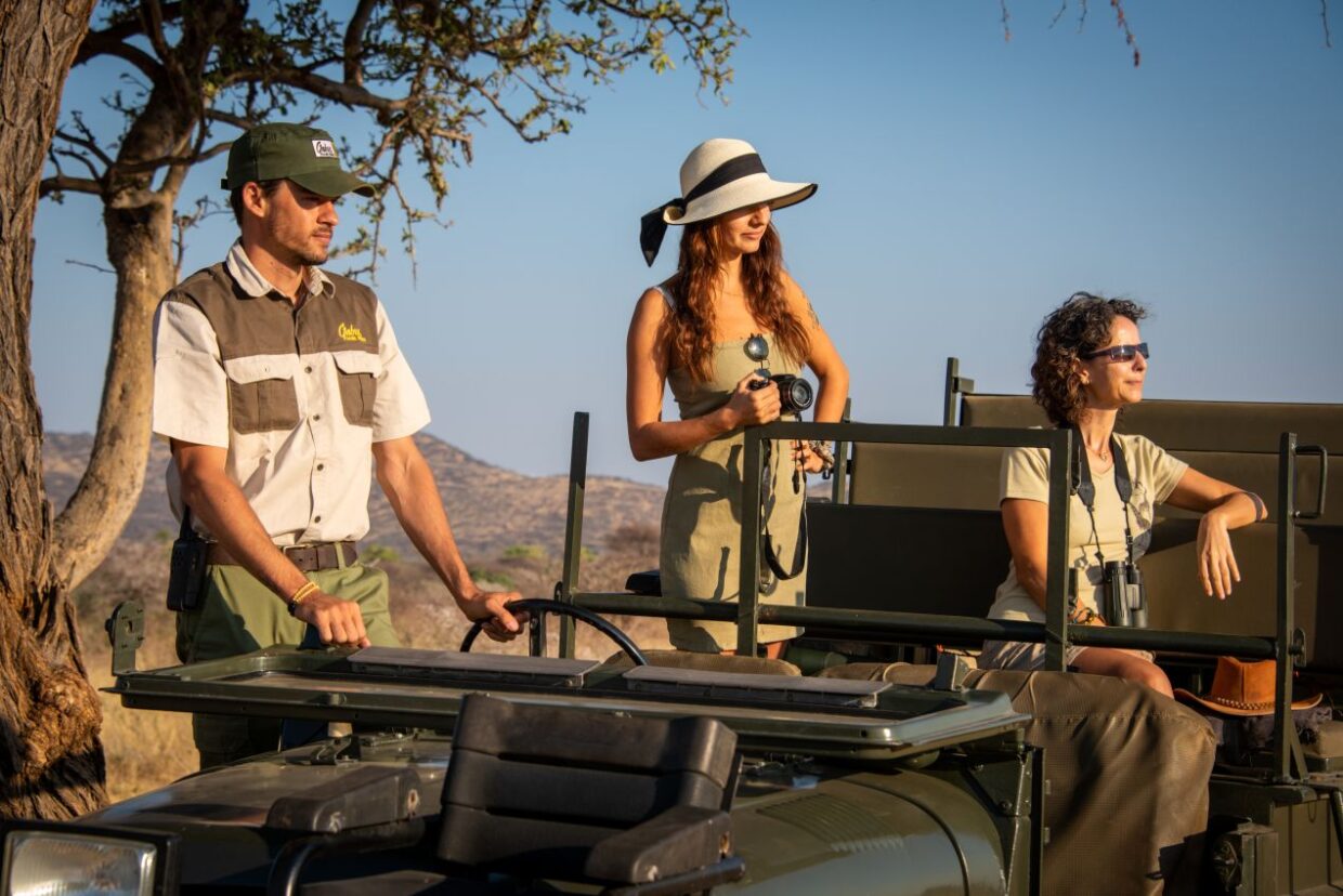 Safari-Gruppe in beiger, funktionaler Kleidung auf einer Pirschfahrt durch Tansania im offenen Geländewagen